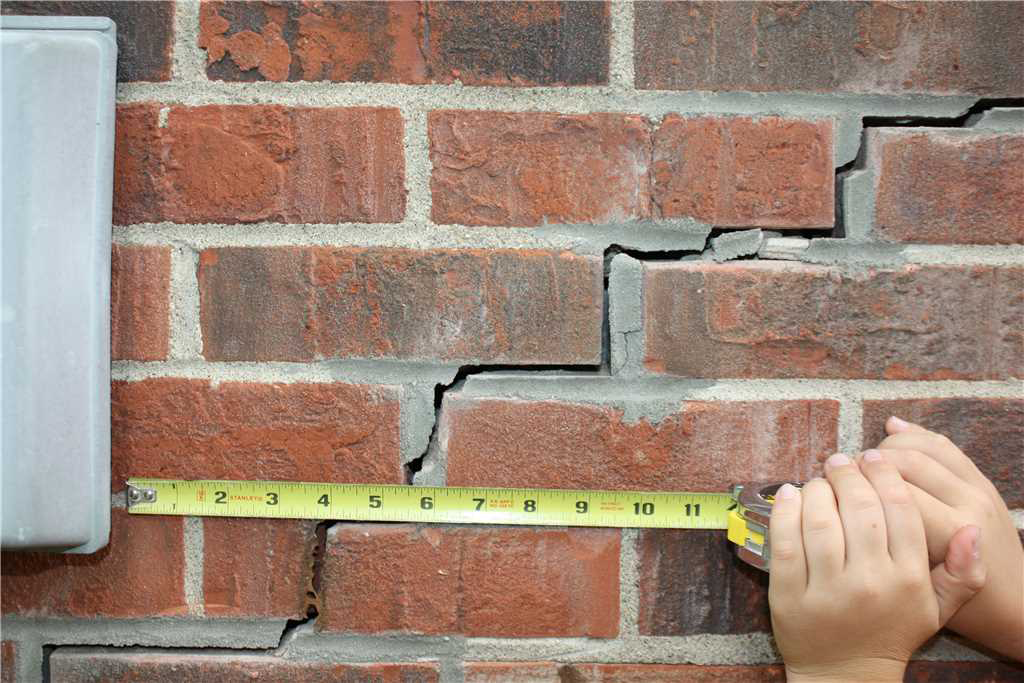 cracked exterior brick wall with tape measure